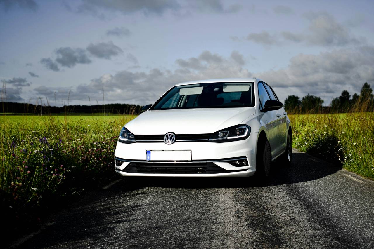 White Volkswagen Golf seen from the front on a country road between fields
