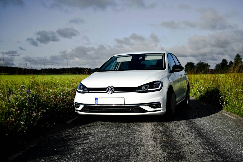 White Volkswagen Golf seen from the front on a country road between fields