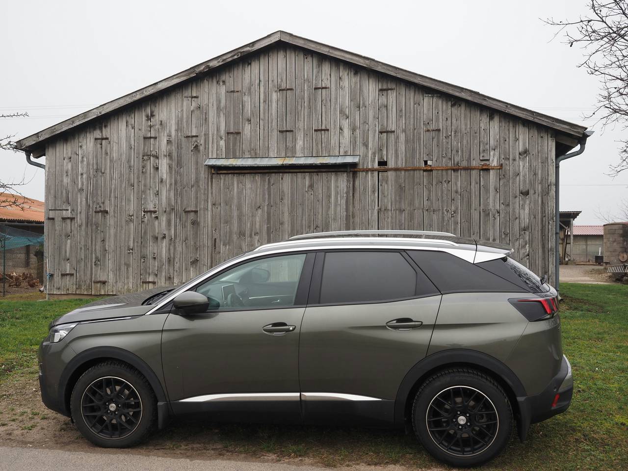 Grey Peugeot SUV seen from the side in front of an old wooden barn