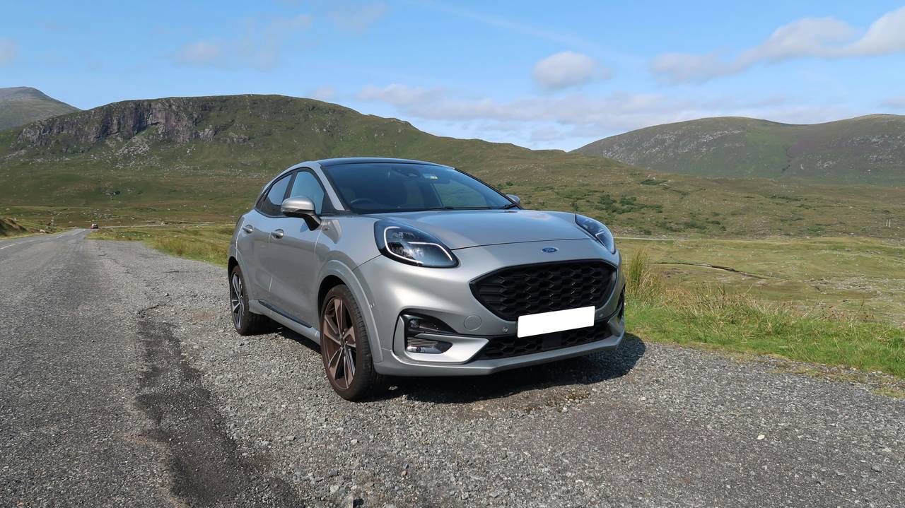Silver Ford Puma seen from the front on gravel with green hills behind