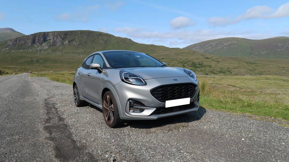 Silver Ford Puma seen from the front on gravel with green hills behind