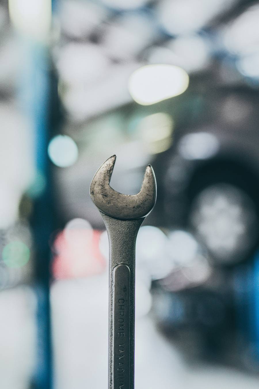 A worn spanner in front of a blurred workshop with a car on a lift