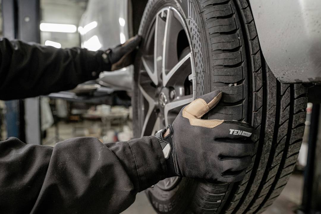 A mechanic in work gloves fitting a wheel to a car
